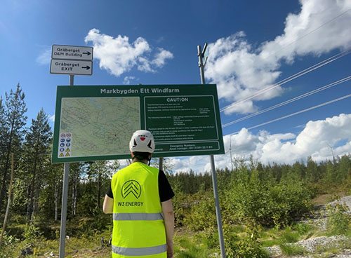 A men in an reflective vest standing in front of a green roadsign